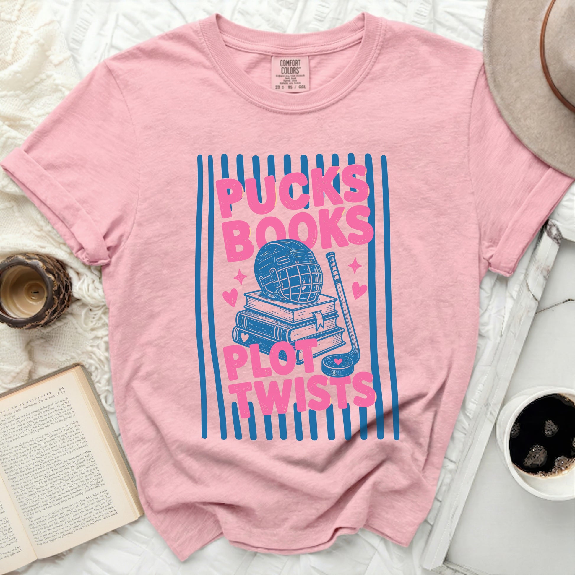 Pink t-shirt with "Pucks, Books, Plot Twists" graphic and hockey elements.