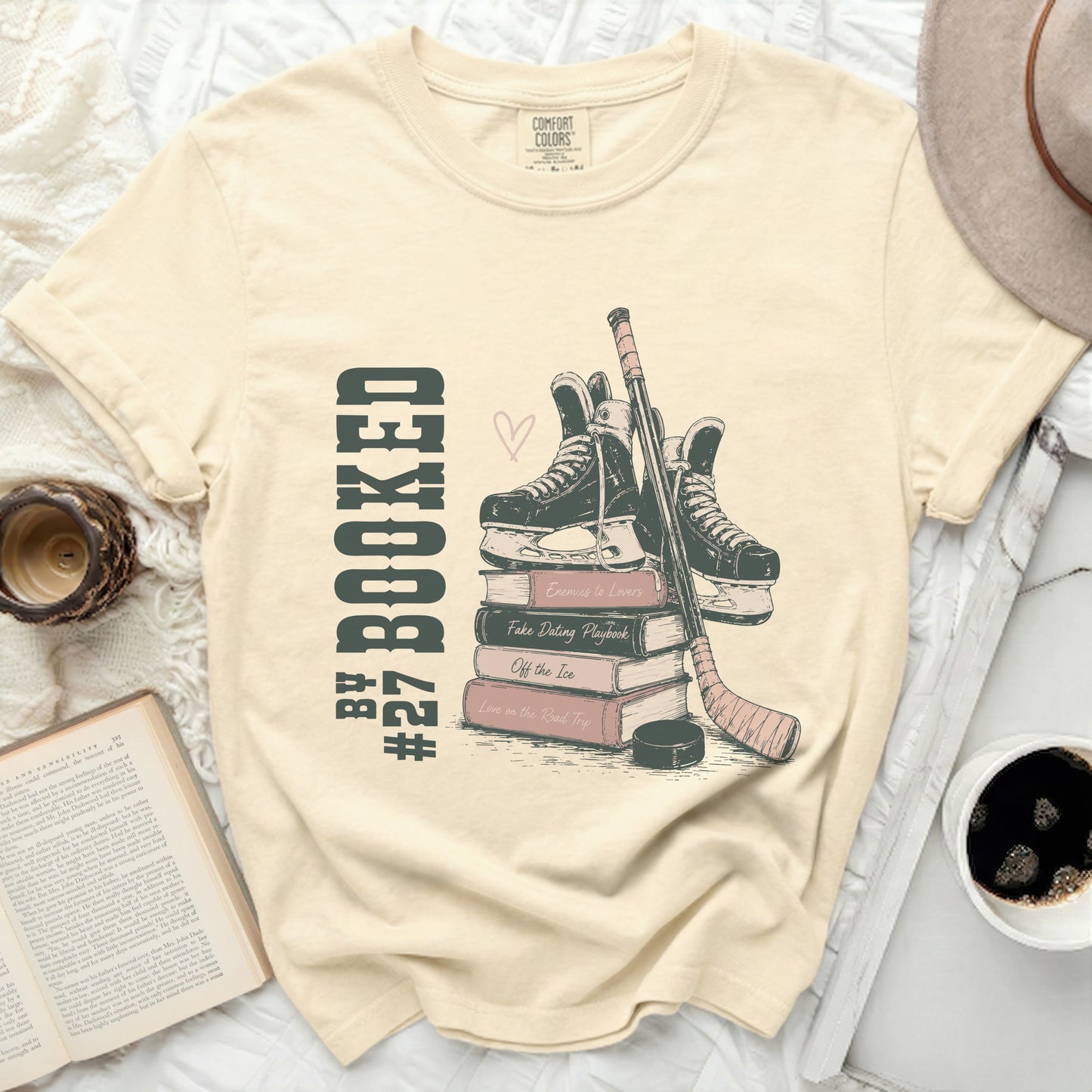 Cream t-shirt with stacked books, ice skates, hockey stick, and puck.