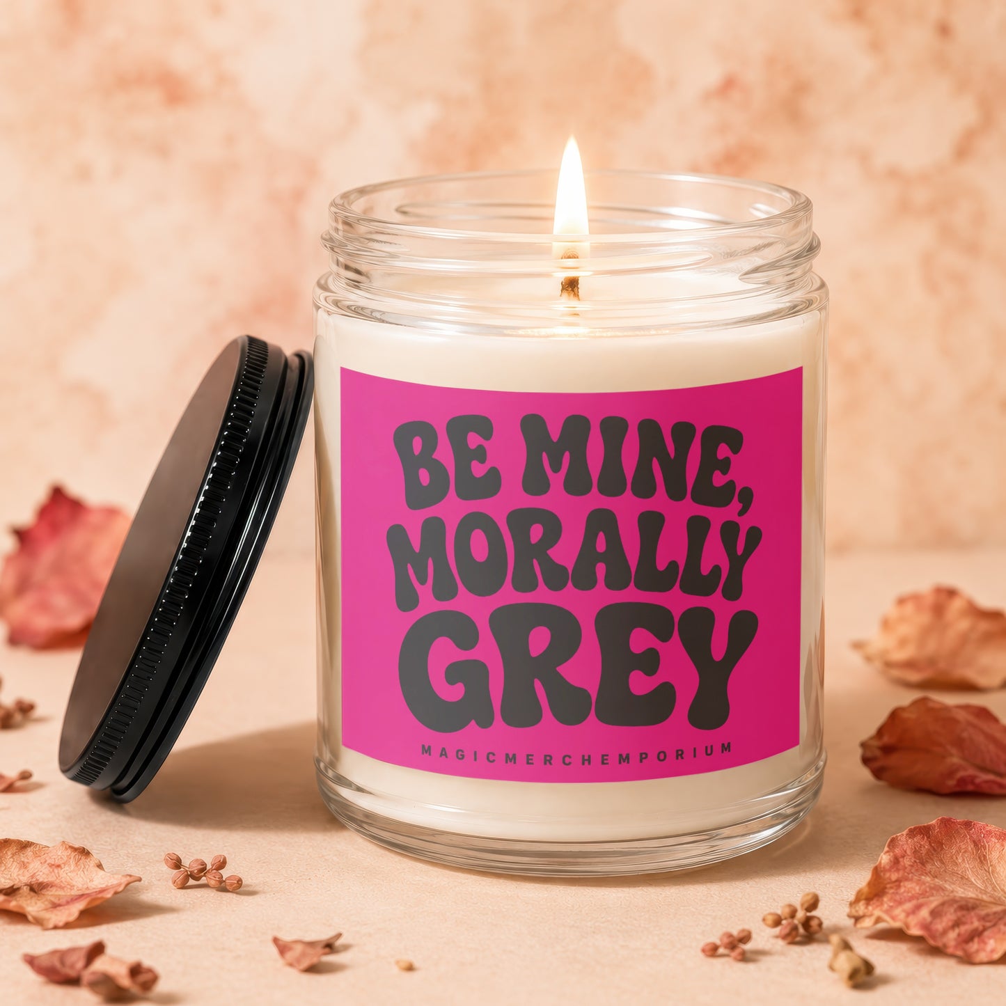 Lit candle in a glass jar with a pink label reading "BE MINE, MORALLY GREY".