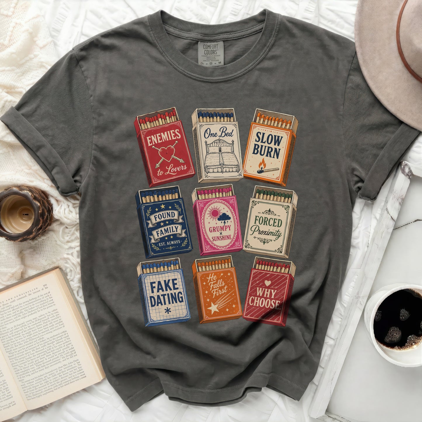 Dark grey t-shirt with matchbox designs: Enemies to Lovers, Slow Burn, Found Family, Grumpy Sunshine, Forced Proximity, Fake Dating, He Falls First, Why Choose.