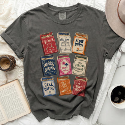 Dark grey t-shirt with matchbox designs: Enemies to Lovers, Slow Burn, Found Family, Grumpy Sunshine, Forced Proximity, Fake Dating, He Falls First, Why Choose.