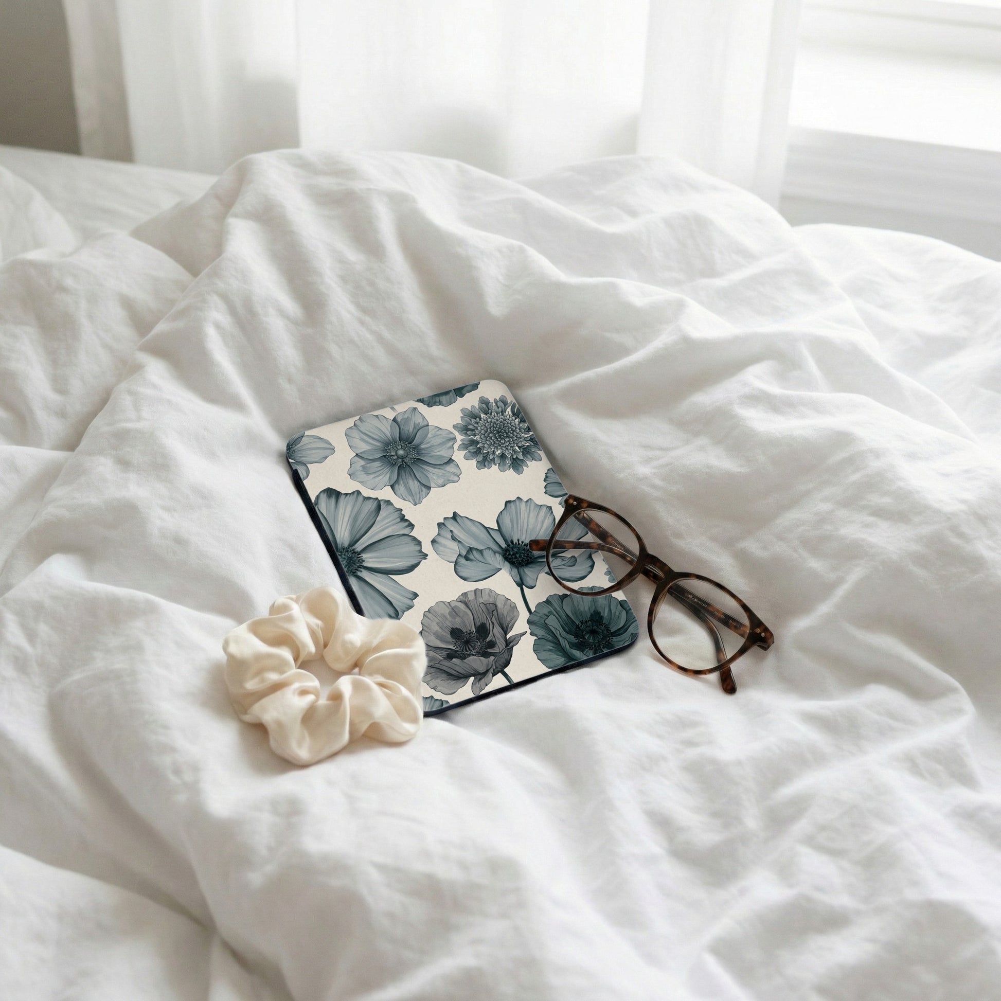 Floral print notebook, scrunchie, and glasses on rumpled white sheets.