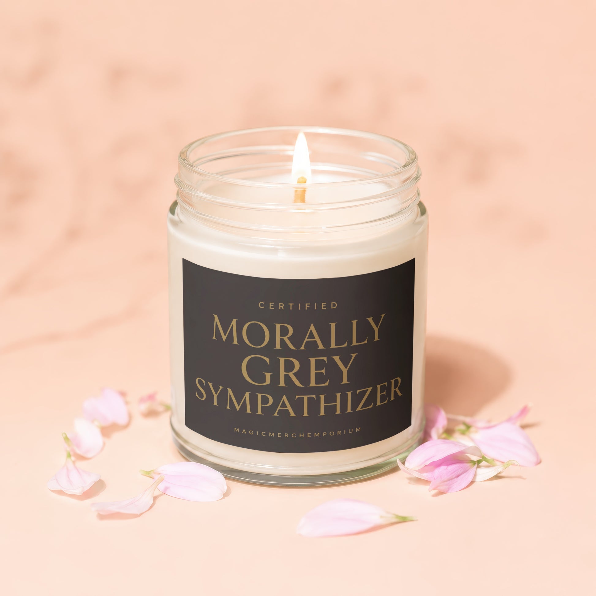Candle with label "Certified Morally Grey Sympathizer" and light petals on peach background.