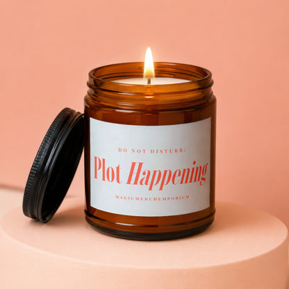 Amber jar candle "Plot Happening" with lit wick and open lid.