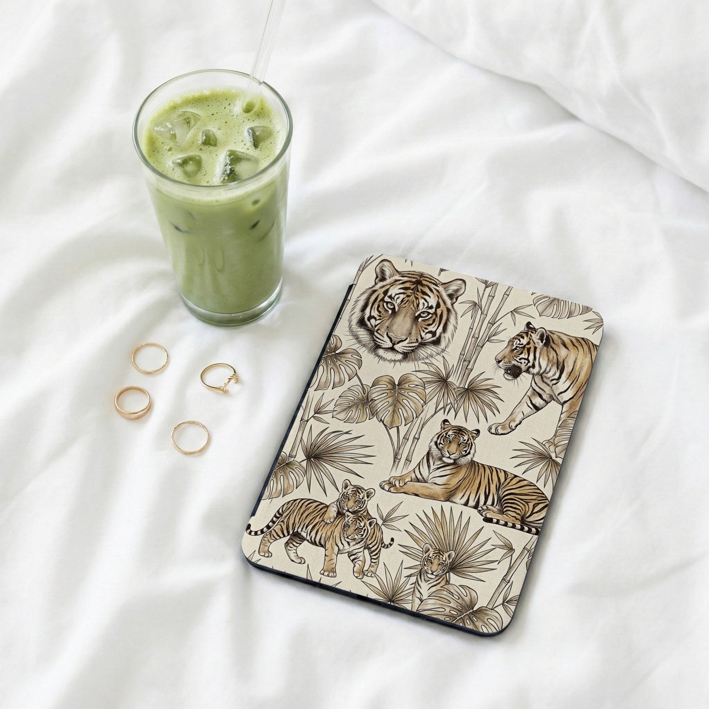 Tablet cover with tigers and tropical leaves, next to iced matcha drink and rings.
