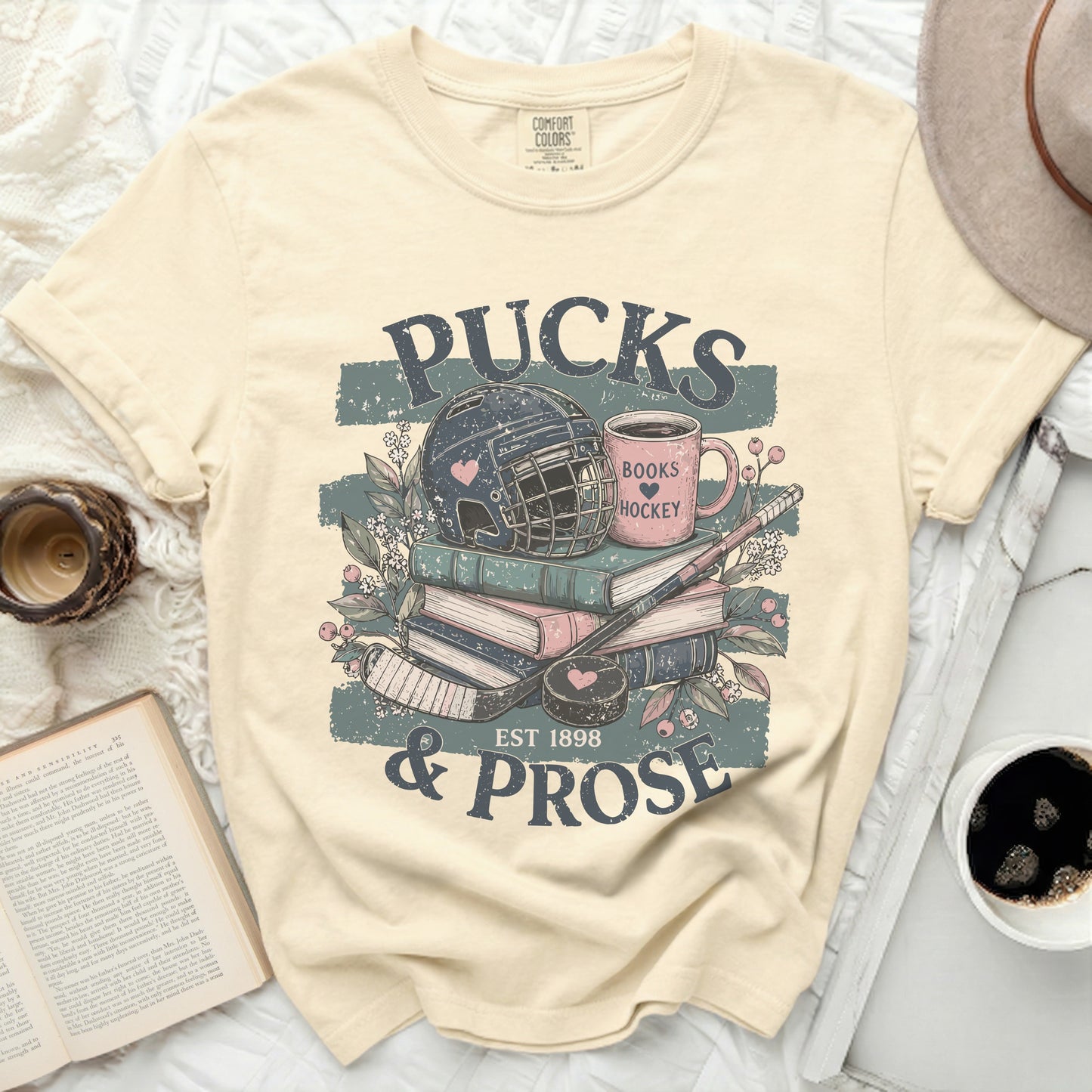 Cream t-shirt with hockey and book graphics and text "PUCKS & PROSE".