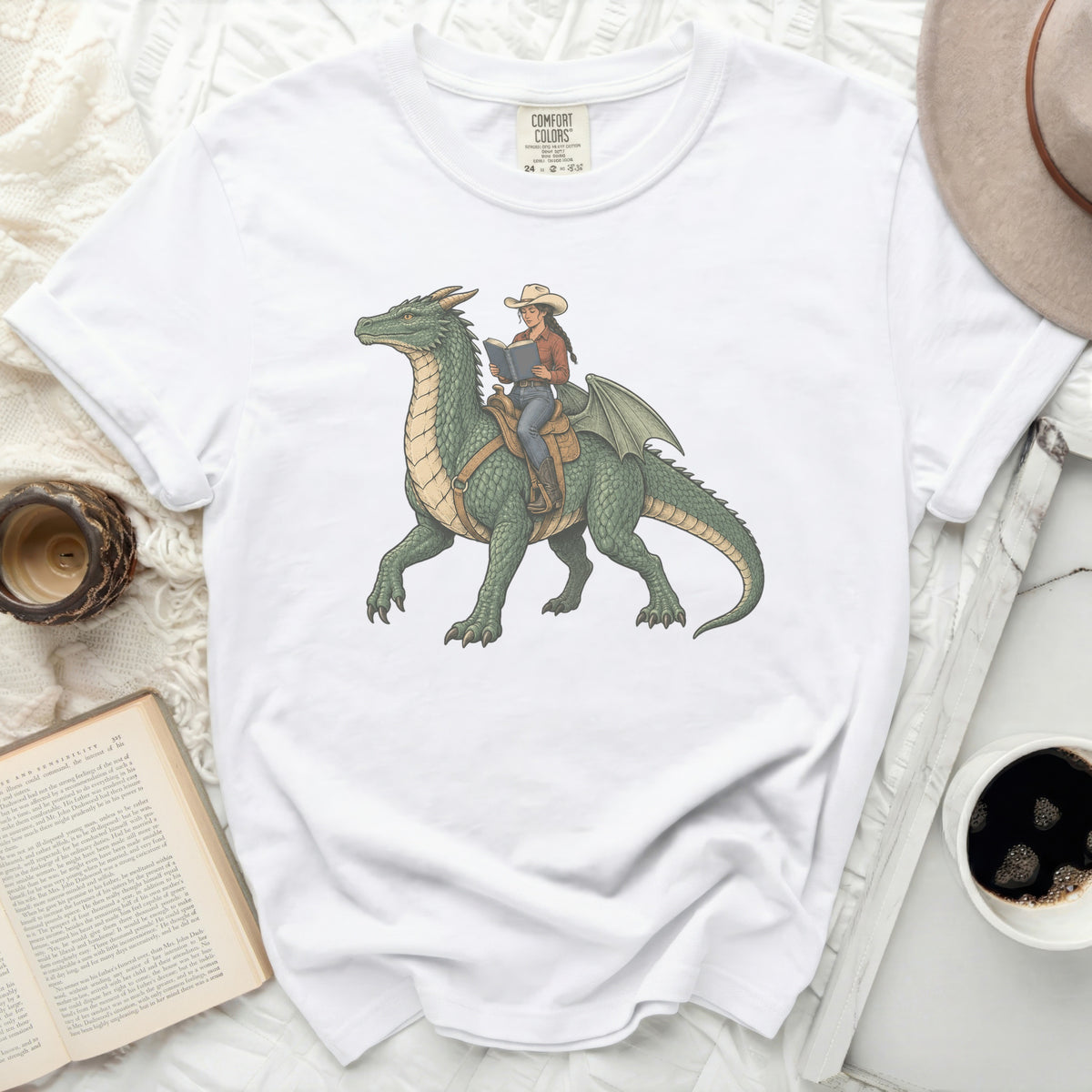 White t-shirt featuring a green dragon with a cowgirl reading a book on its back.