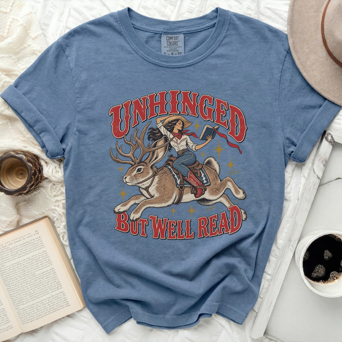 Unhinged but well read graphic of cowgirl riding a jackalope, holding a book.