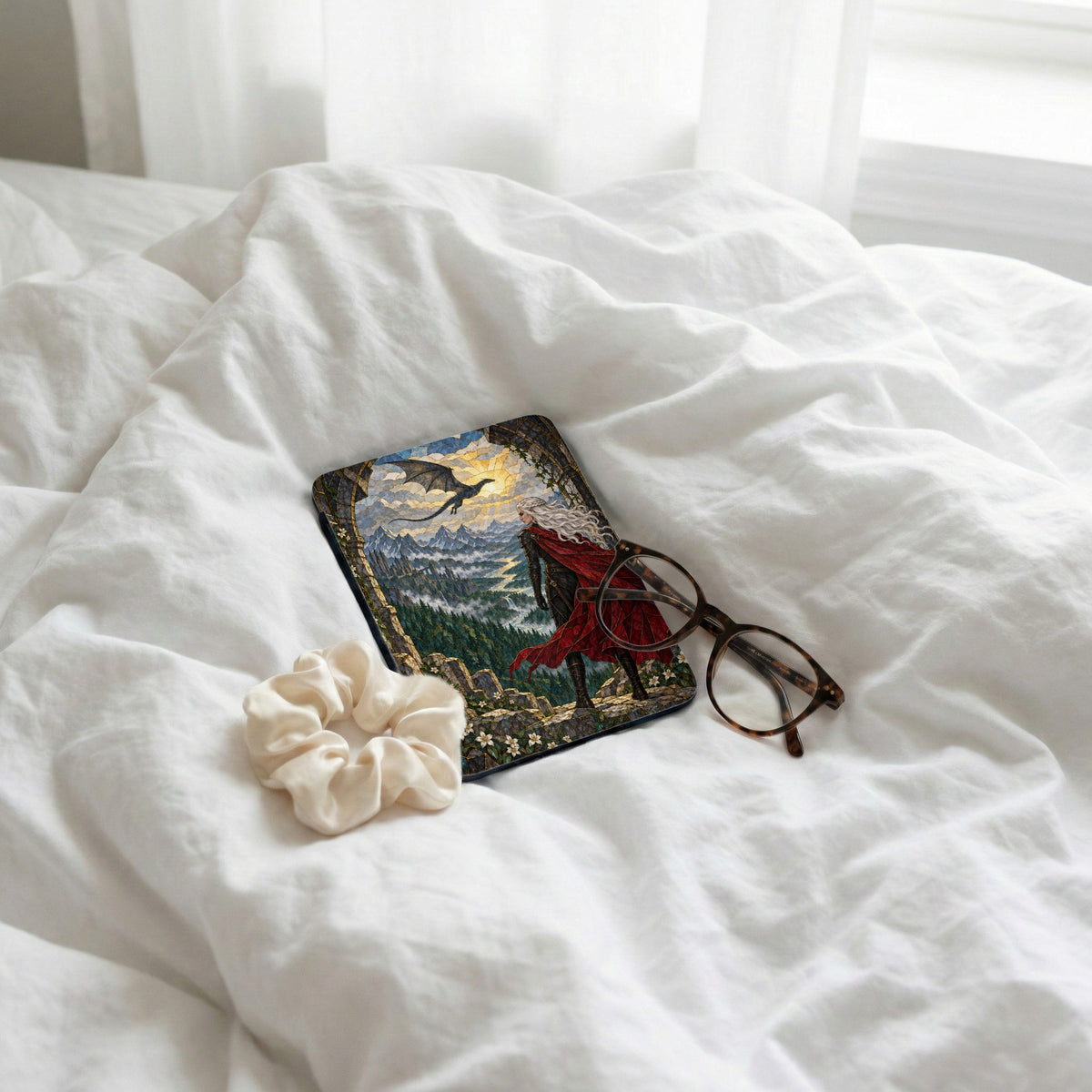 Mousepad with dragon and person in red cape on landscape, next to glasses and scrunchie.