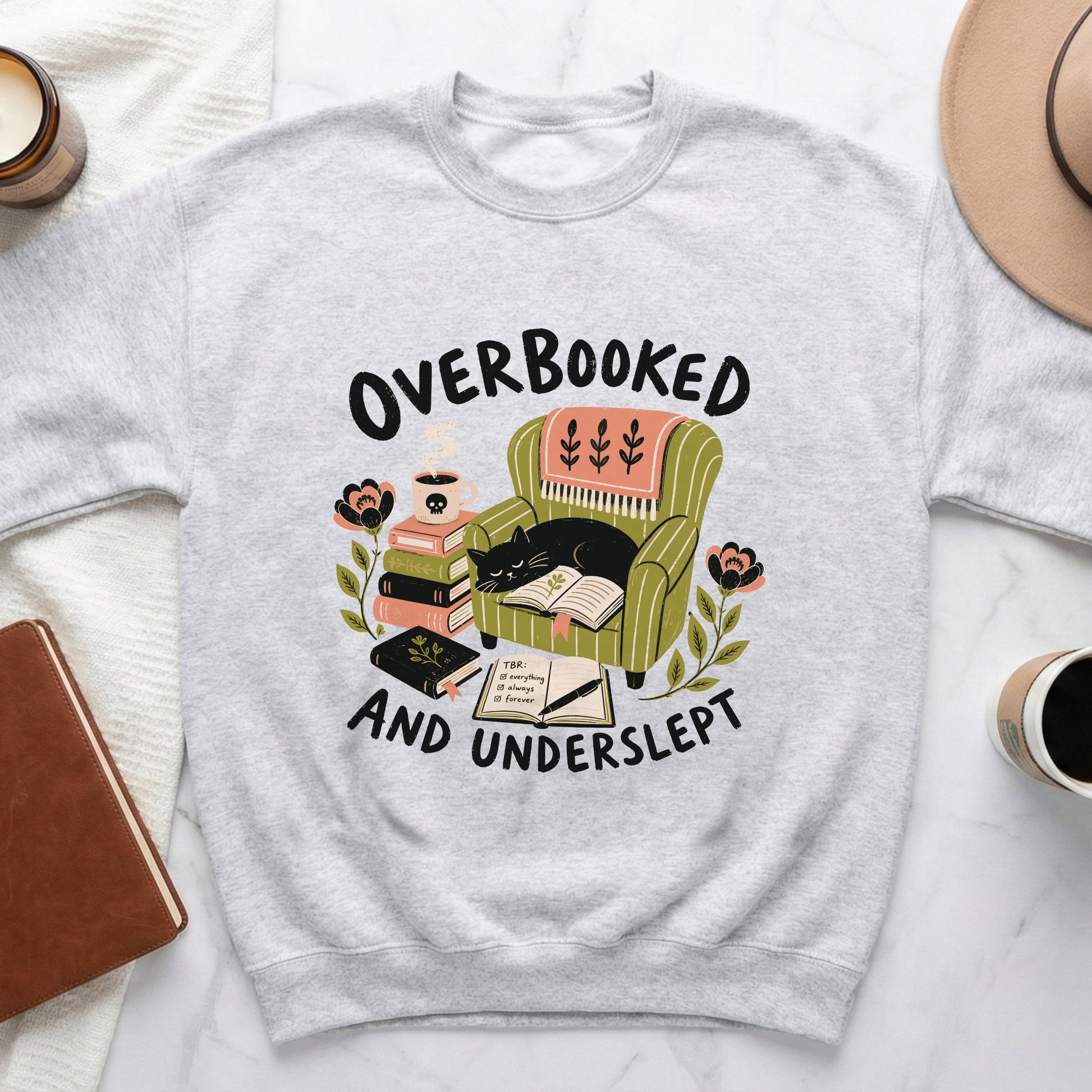 Light gray sweatshirt with illustration "Overbooked and Underslept" and a cat sleeping.