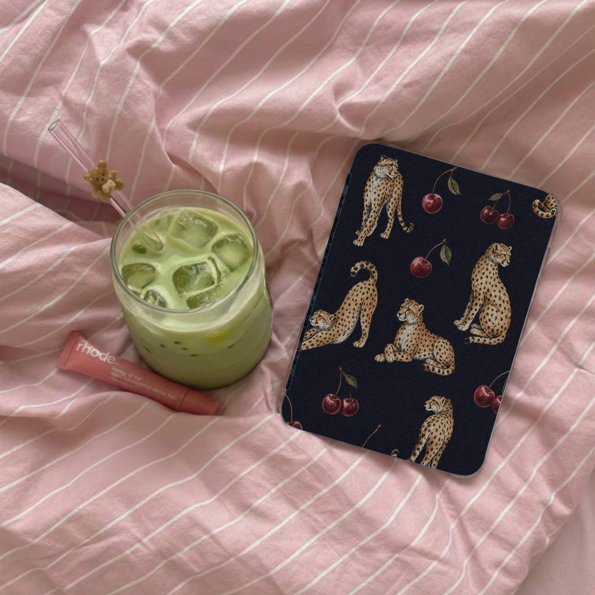 Dark blue case with cheetahs and cherries pattern next to green drink.