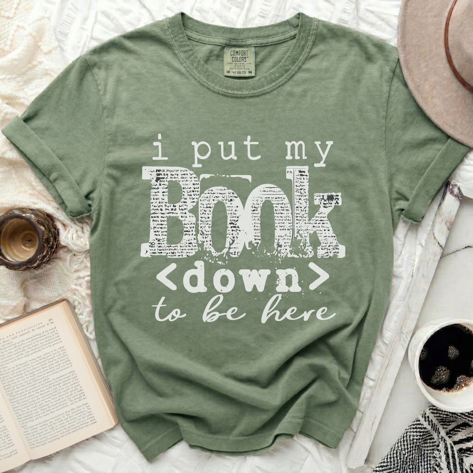 Olive green t-shirt with white text \"i put my BOOK <down> to be here\".