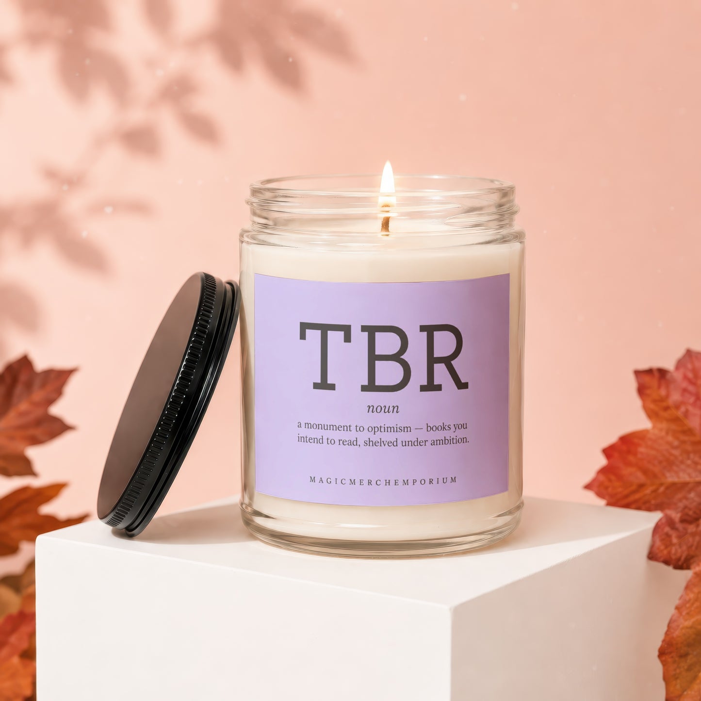 Lit candle in a glass jar with a purple label reading "TBR" and its definition.