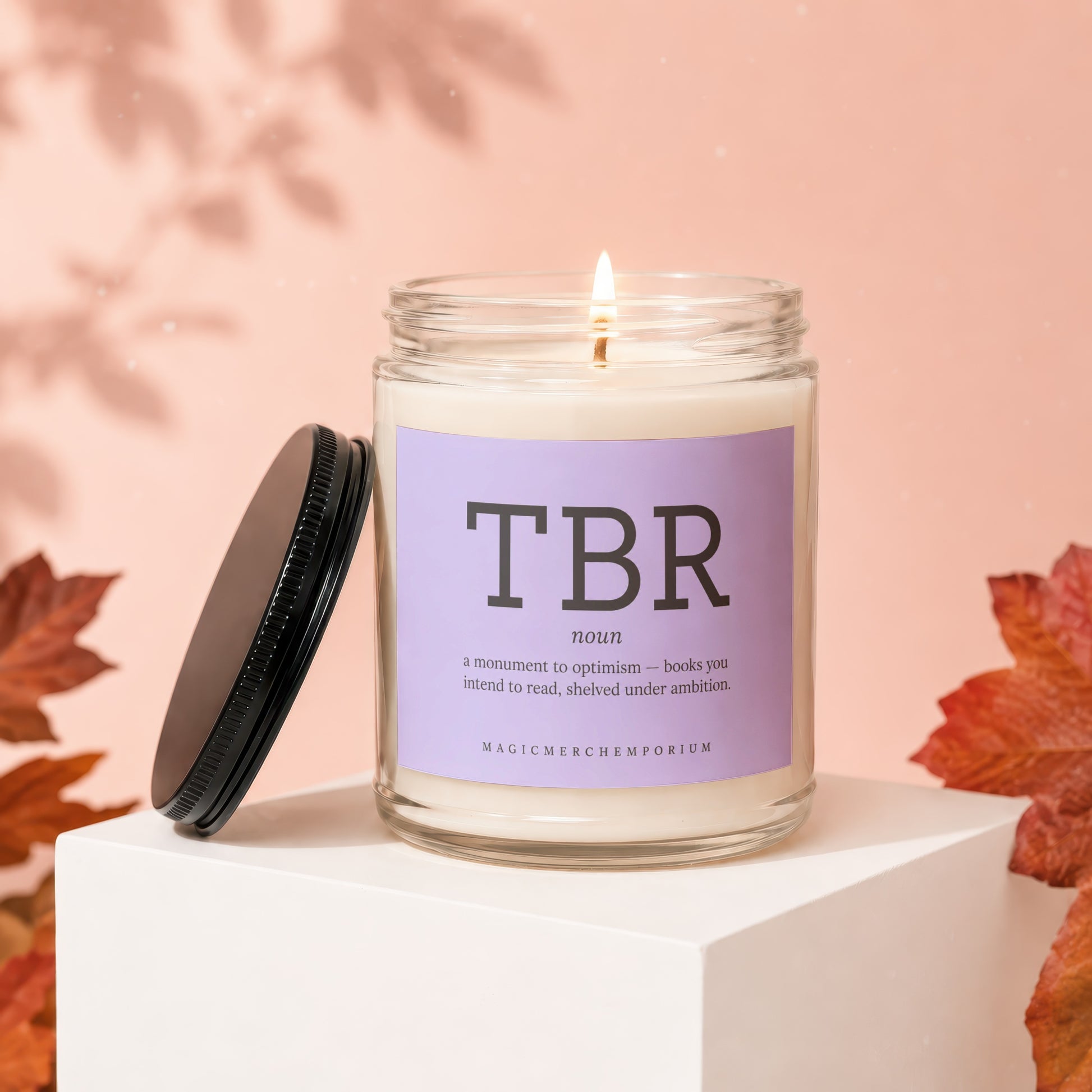 Lit candle in a glass jar with a purple label reading "TBR" and its definition.