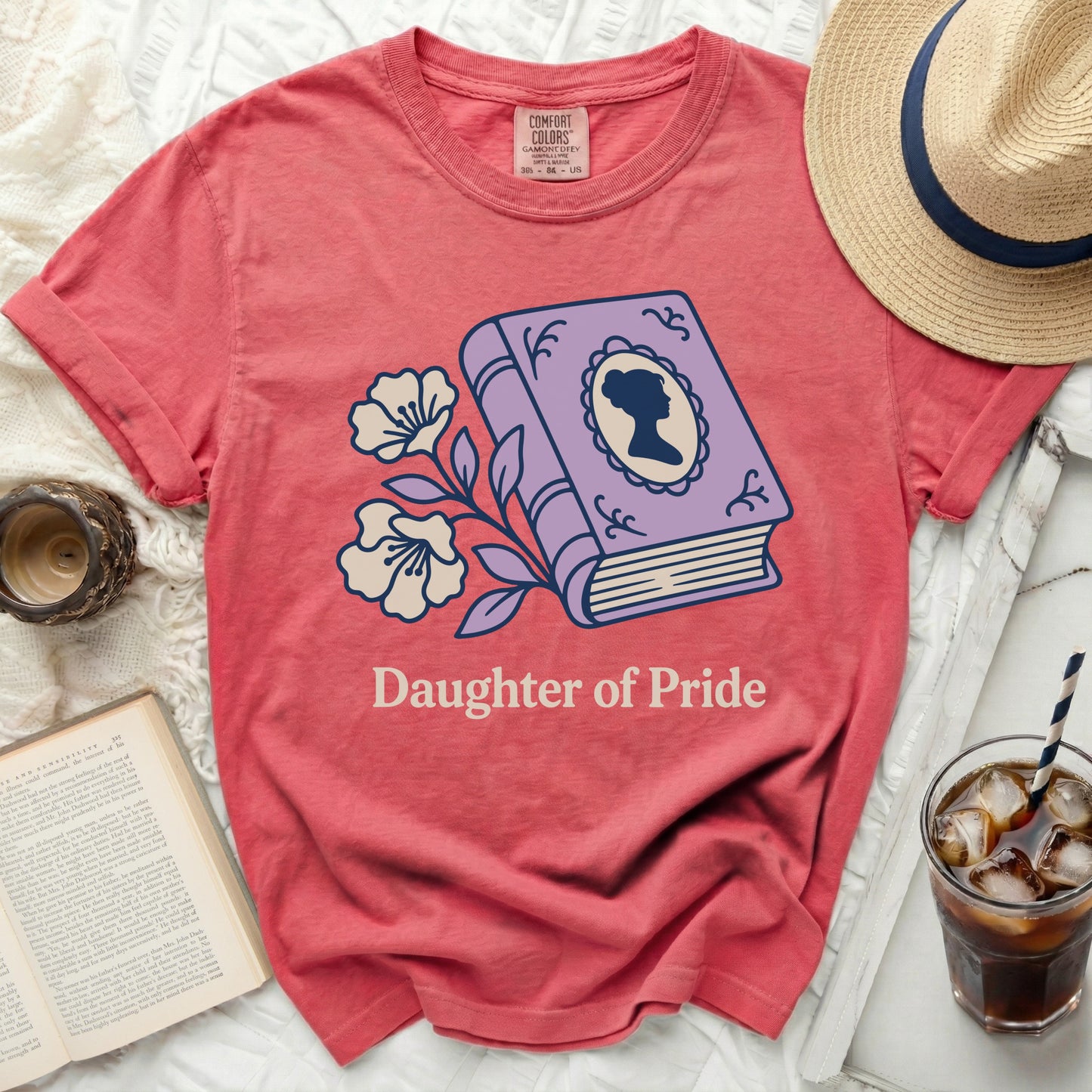 Coral t-shirt with purple book, flowers, and "Daughter of Pride" text.