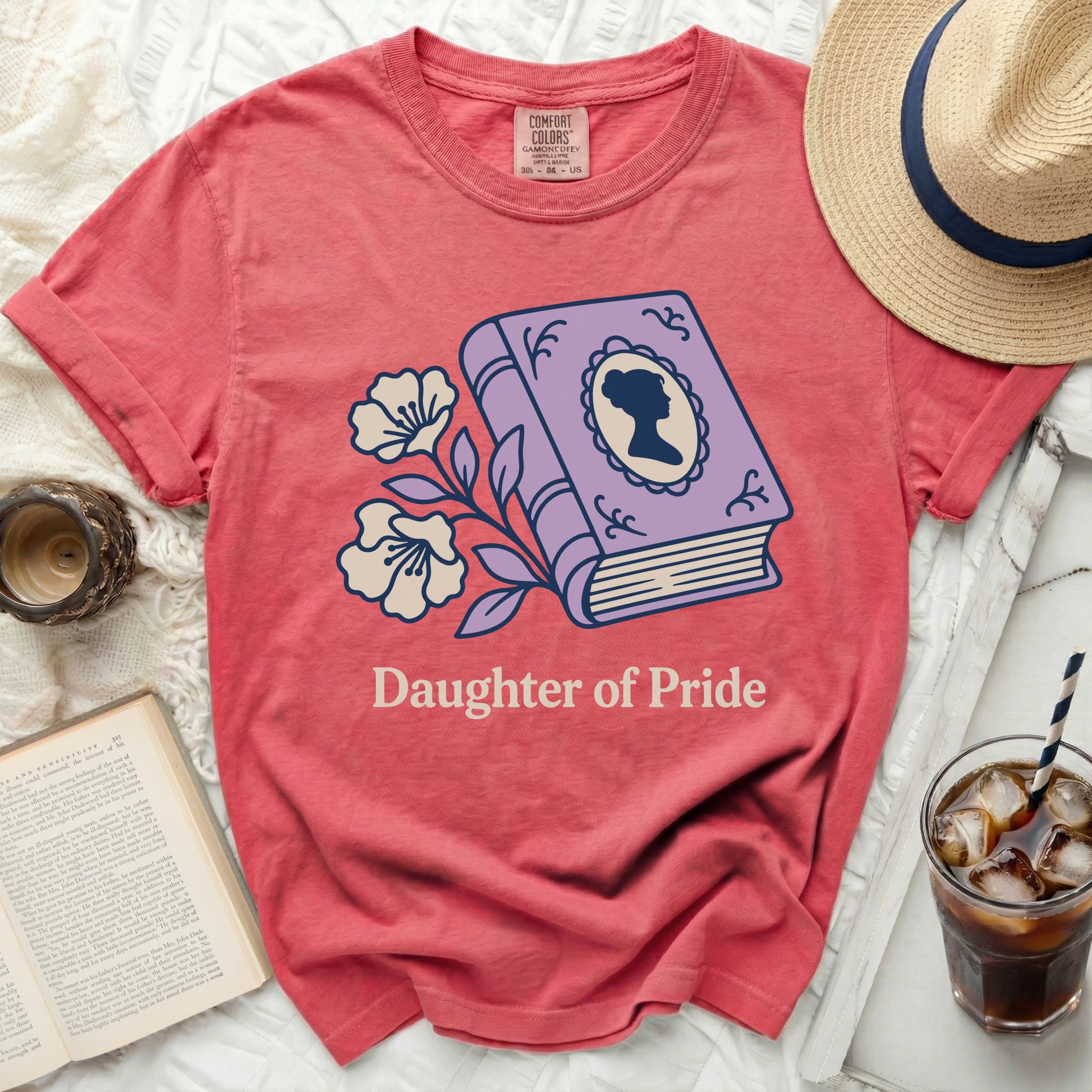 Coral t-shirt with purple book, flowers, and "Daughter of Pride" text.