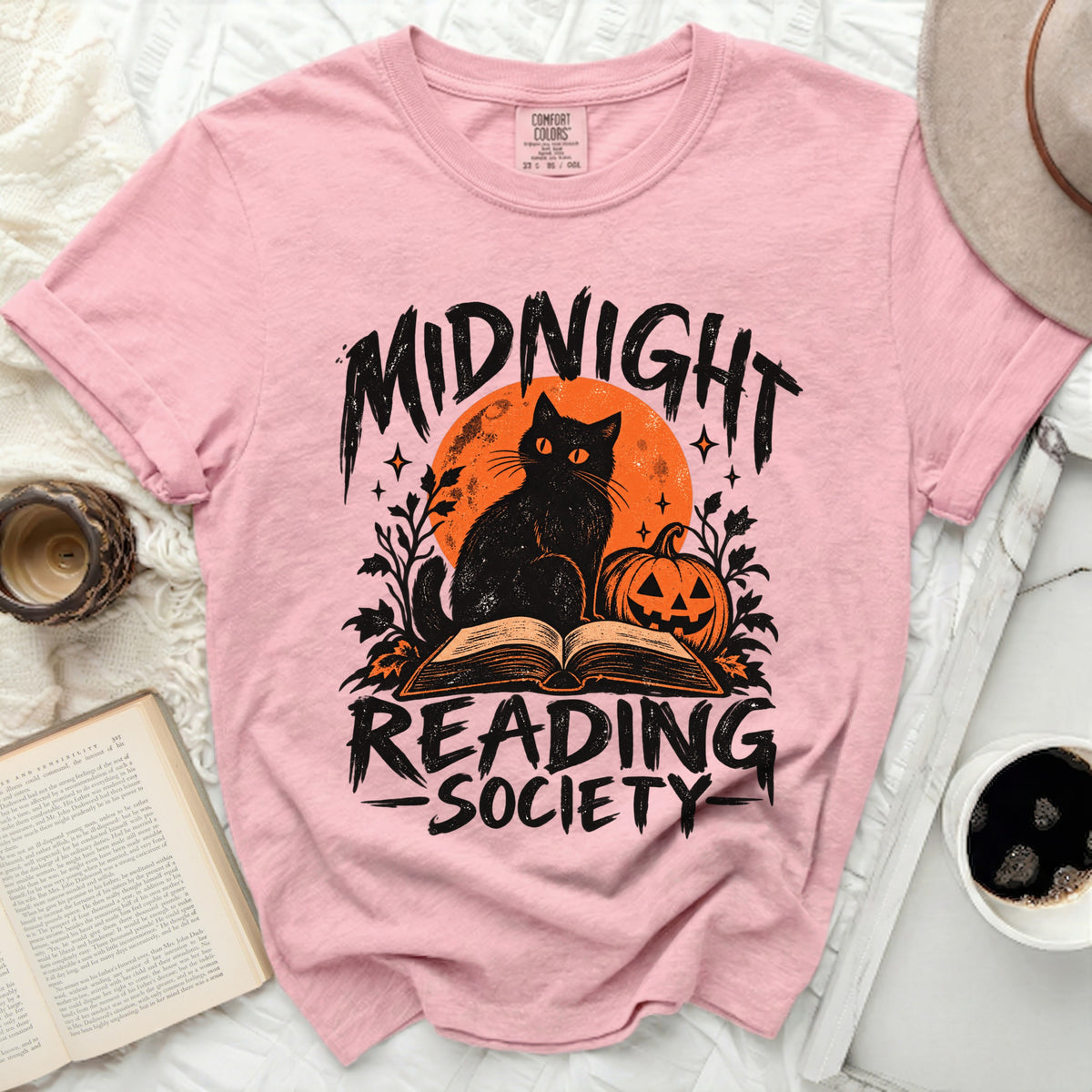 Pink shirt with graphic of black cat, pumpkin, and book, reading "Midnight Reading Society".