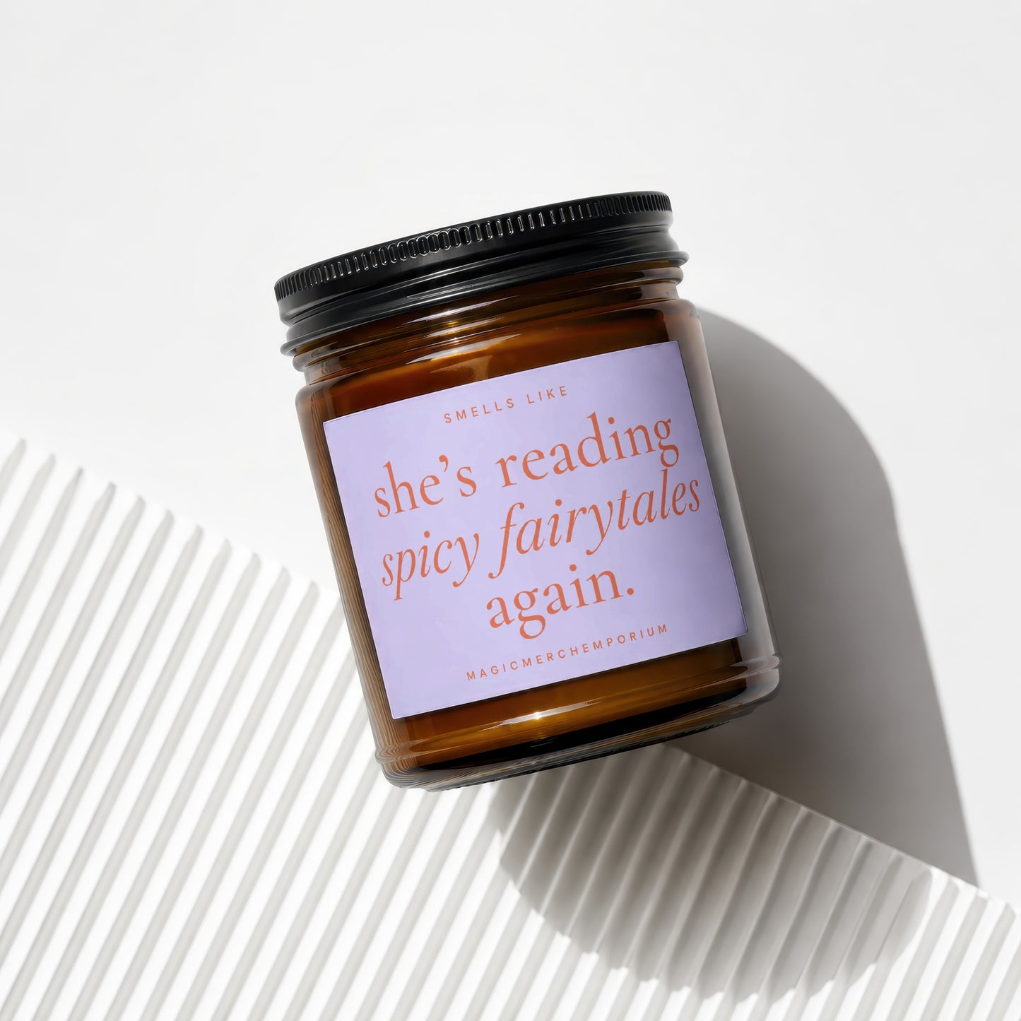 Amber glass candle with black lid, reads "smells like she's reading spicy fairytales again."