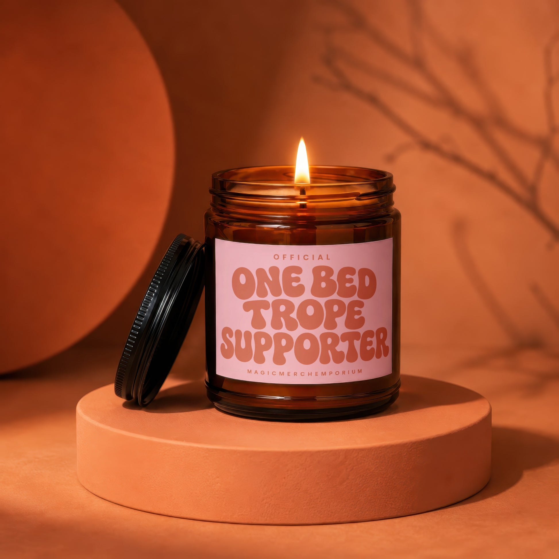 Amber jar candle with lid off and lit, reading "Official One Bed Trope Supporter".