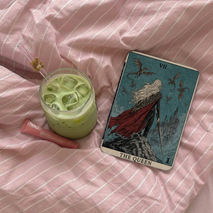 Green iced drink and Rhode lip balm beside a Queen of Wands tarot card.