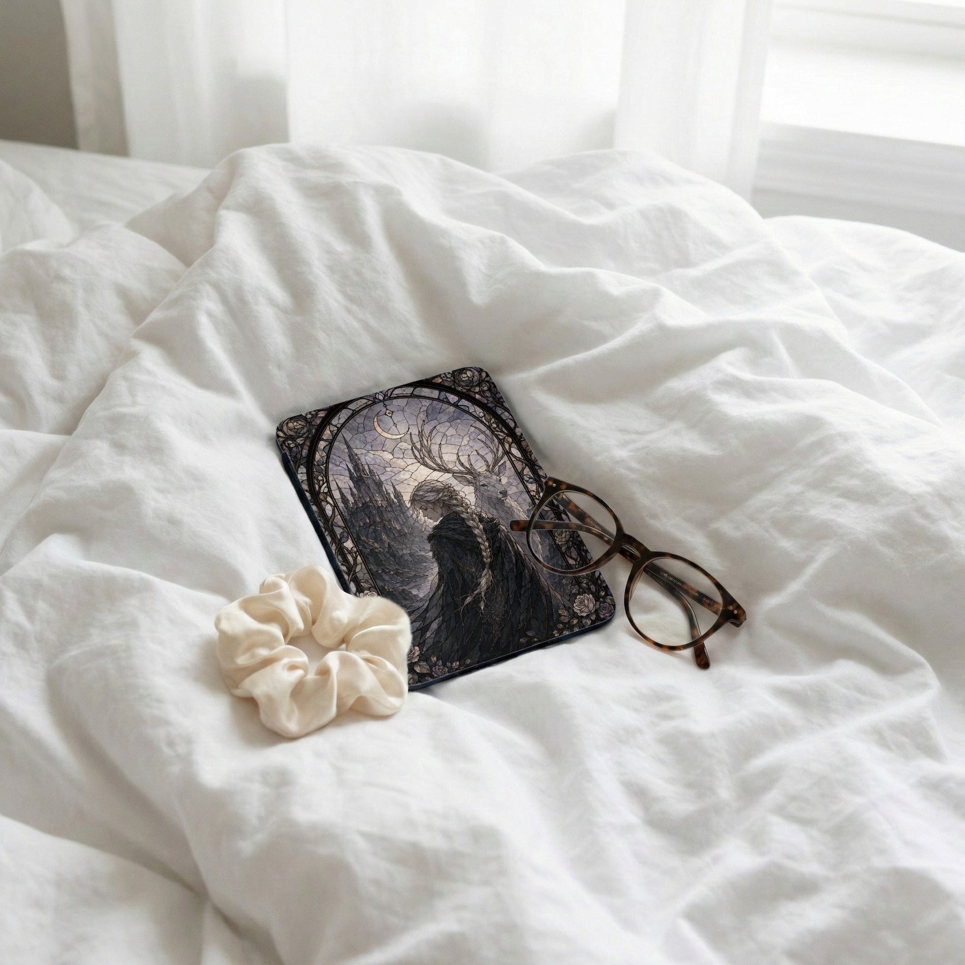 Dark fantasy art case with deer and castle next to glasses and scrunchie.