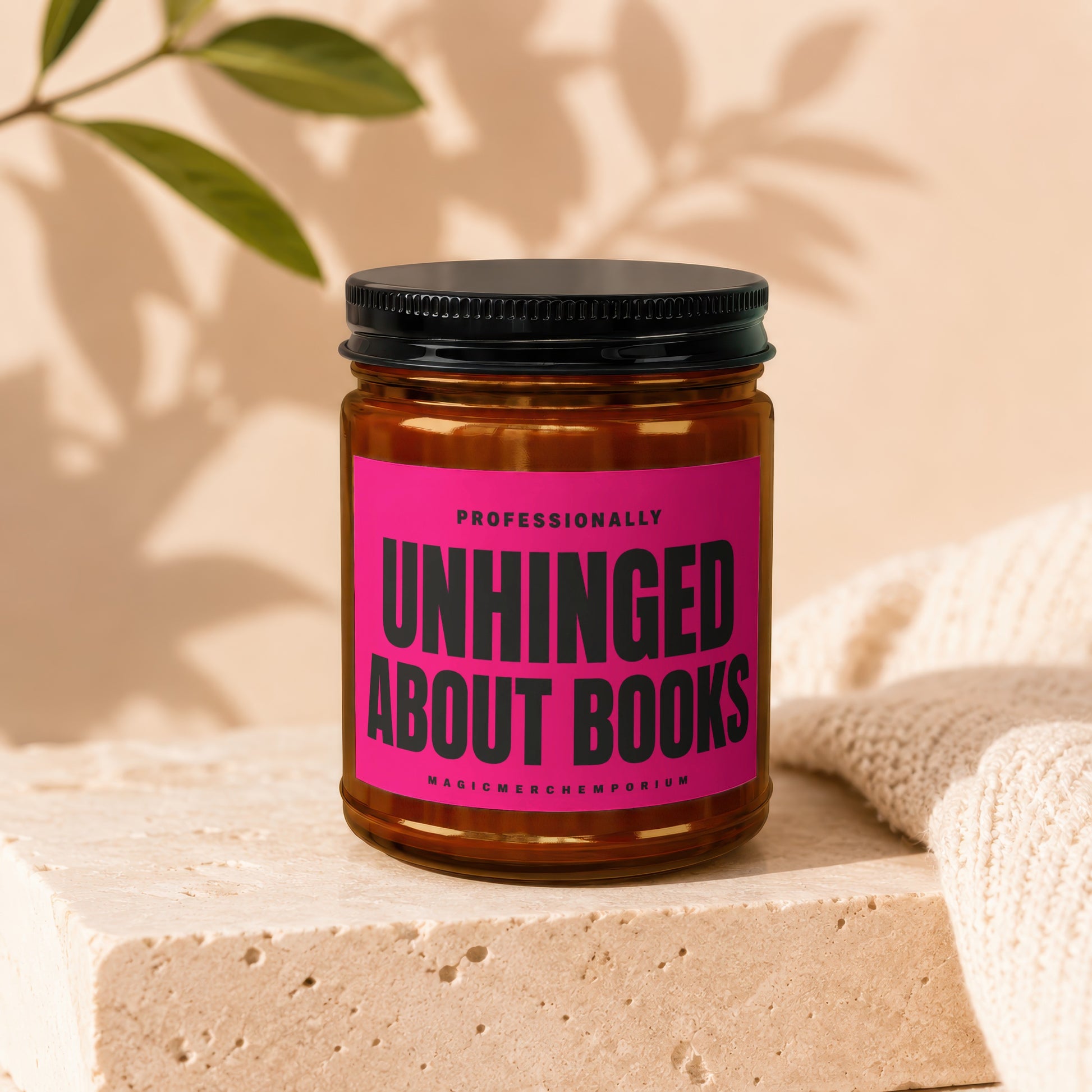 Amber jar candle with black lid and pink label reading "UNHINGED ABOUT BOOKS".