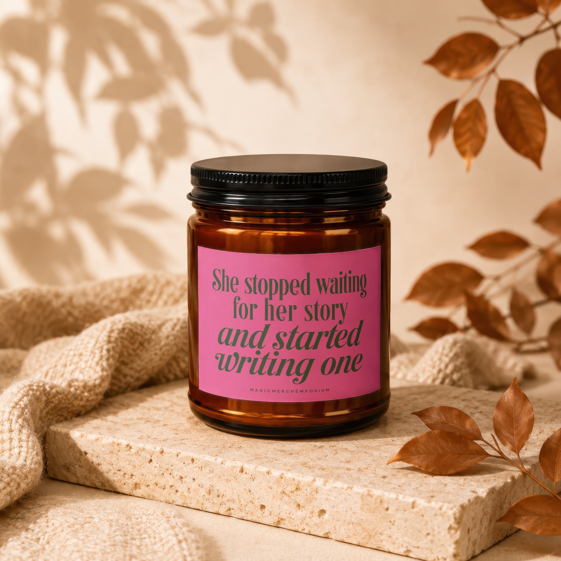 Brown candle with pink label reading "She stopped waiting for her story and started writing one".