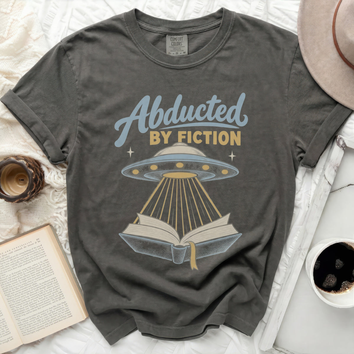 "Abducted by Fiction" text with UFO beaming light onto an open book.
