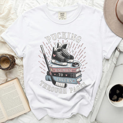 White t-shirt with "Pucking Through Pages" text, hockey skates, and books.