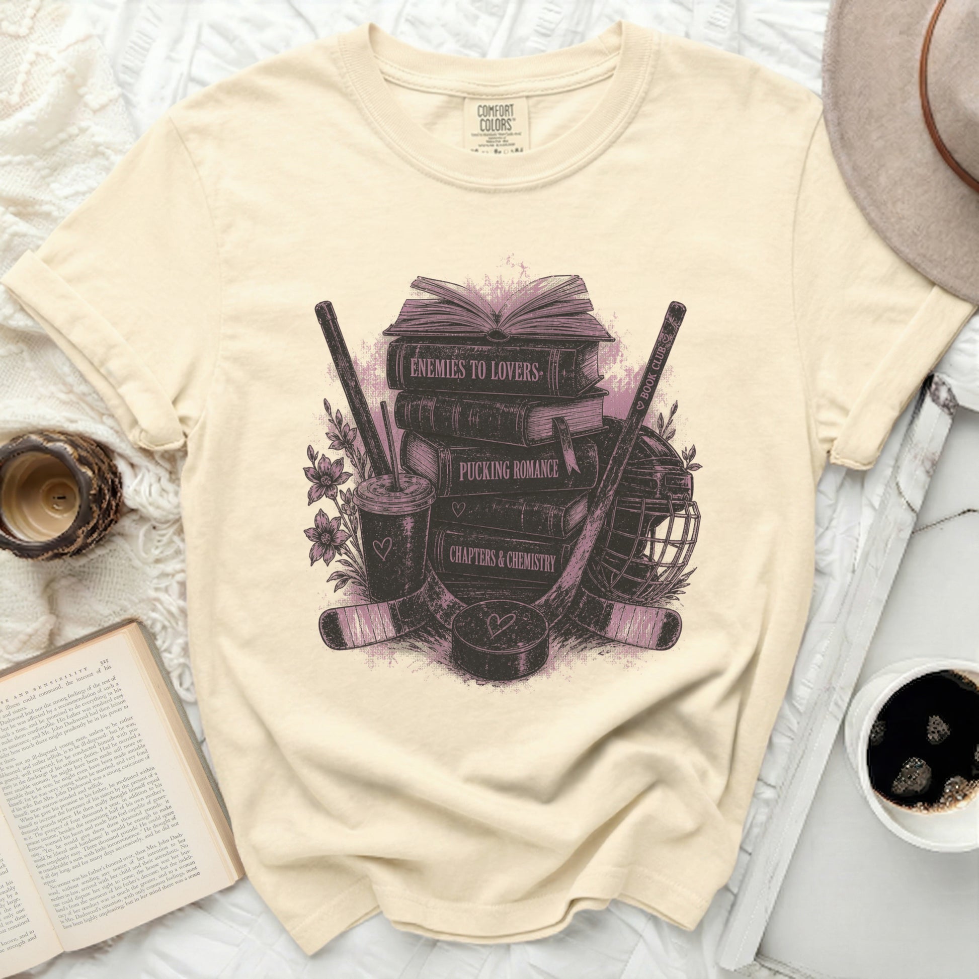 Cream t-shirt with books, hockey sticks, and "Enemies to Lovers" text.