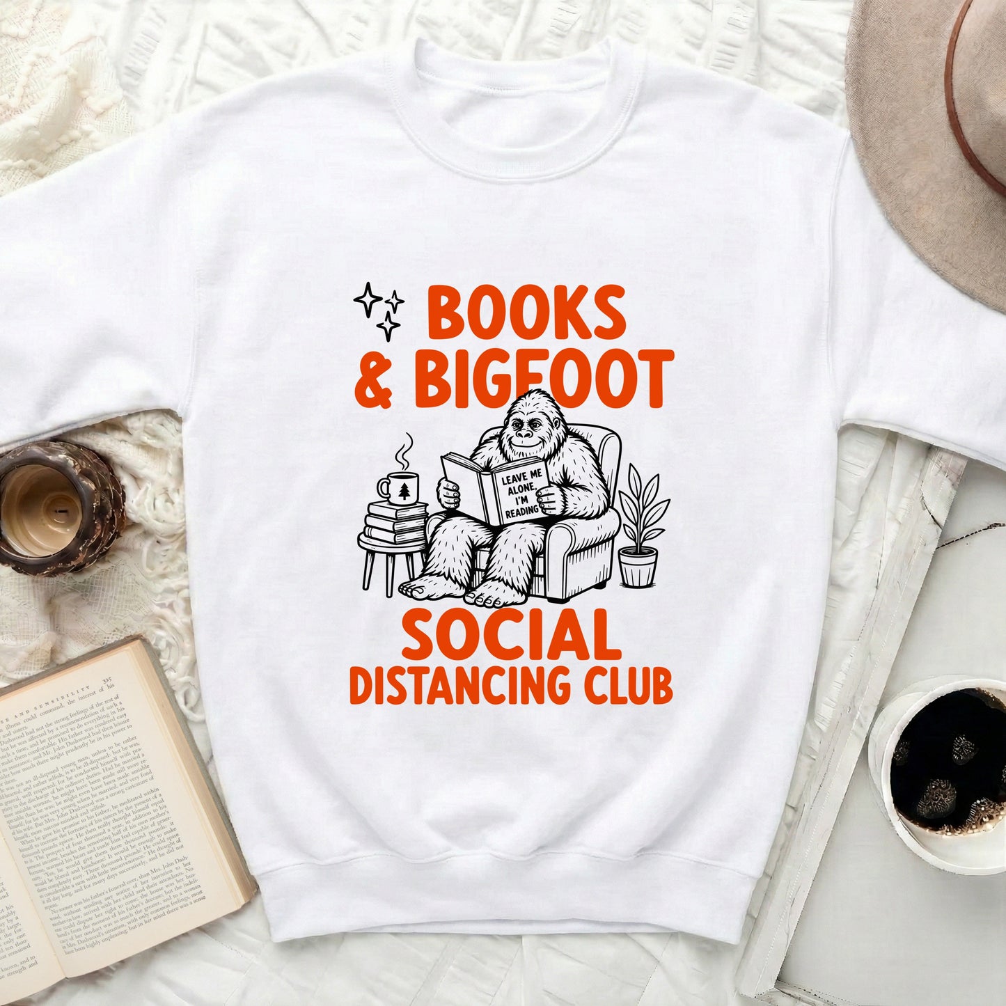 White sweatshirt with "BOOKS & BIGFOOT SOCIAL DISTANCING CLUB" graphic.
