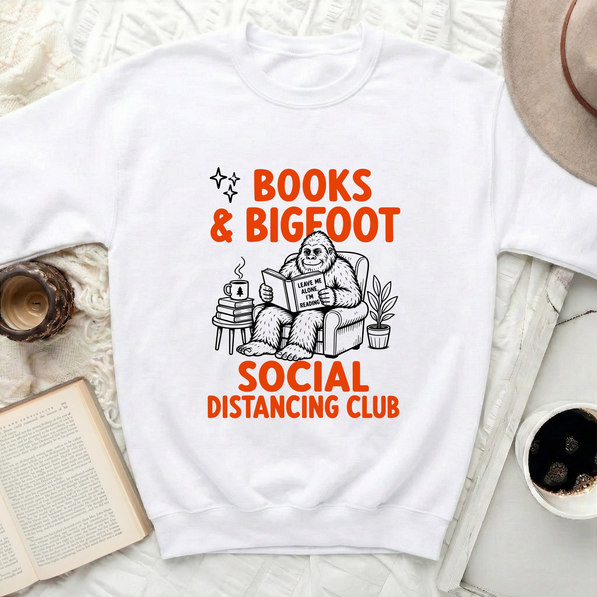 White sweatshirt with "BOOKS & BIGFOOT SOCIAL DISTANCING CLUB" graphic.