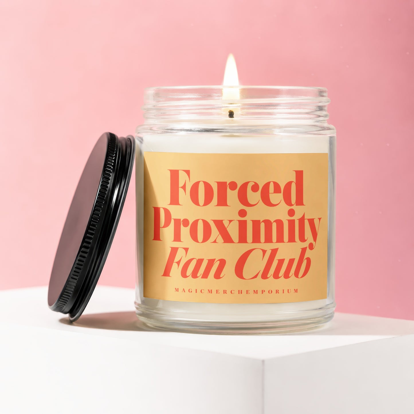 Glass candle with lit wick and black lid, reading "Forced Proximity Fan Club."