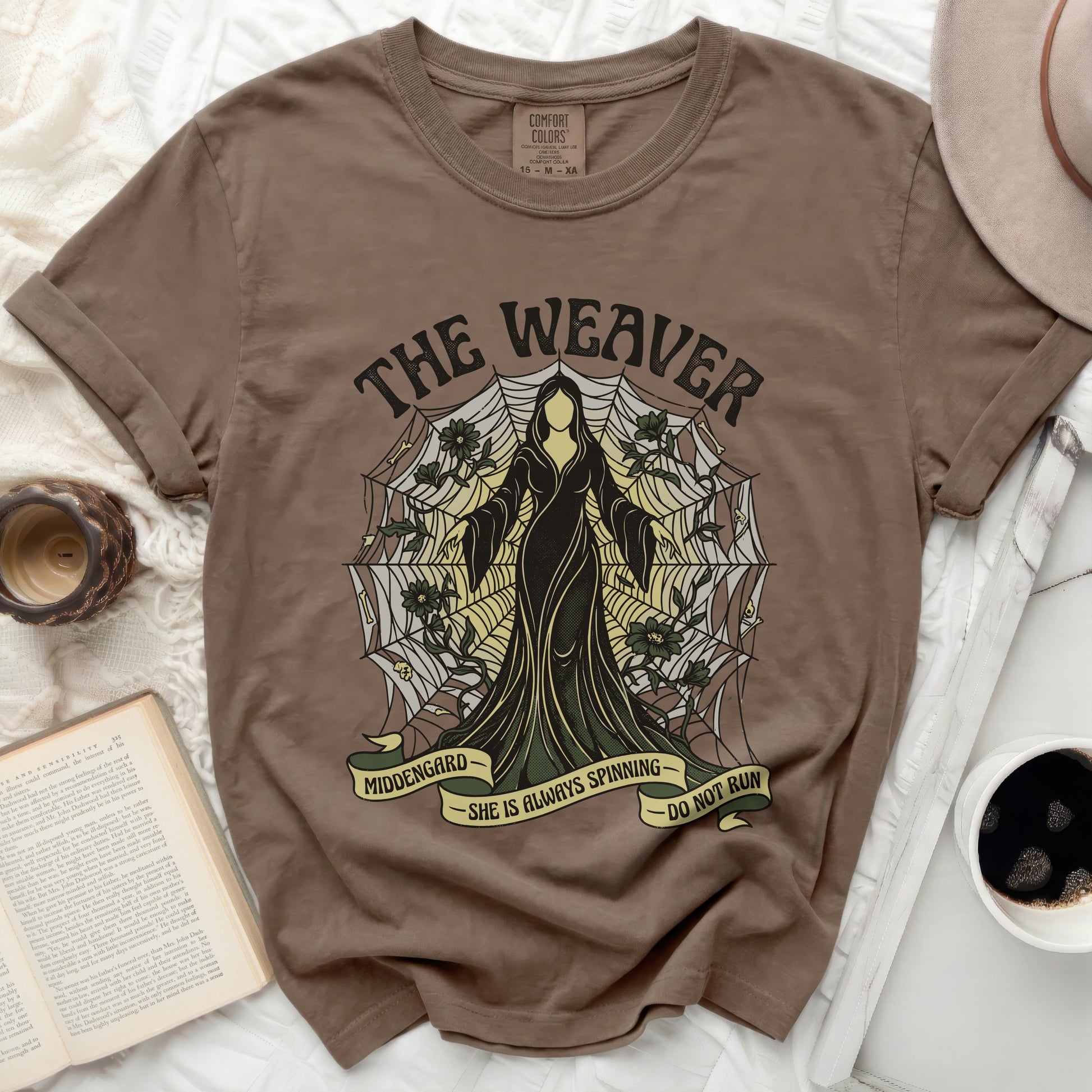 Brown t-shirt with "The Weaver" graphic, spiderweb, and "She is always spinning" text.
