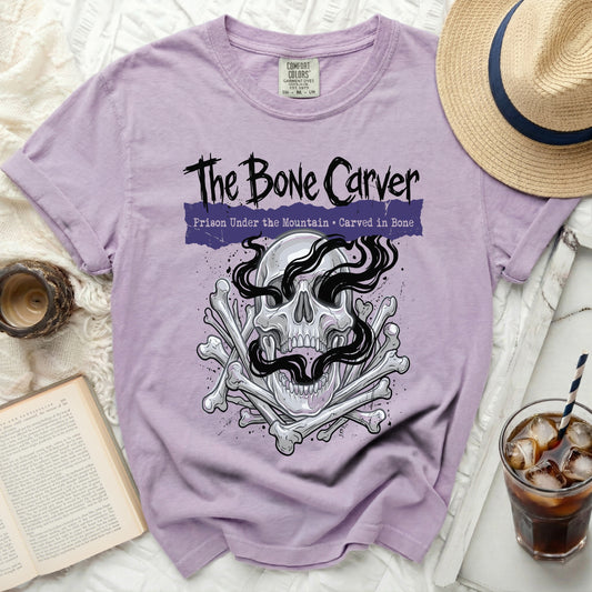 Lavender t-shirt with "The Bone Carver" skull and bones graphic and text.