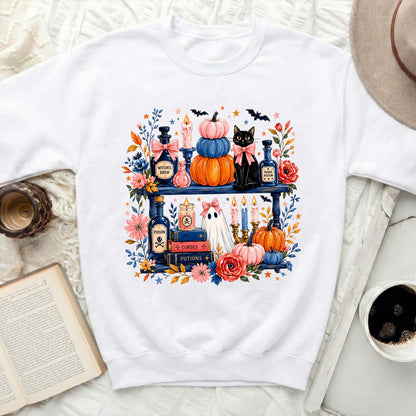 White crewneck sweatshirt with a watercolor Halloween shelf graphic including a black cat, pumpkins, and potions.
