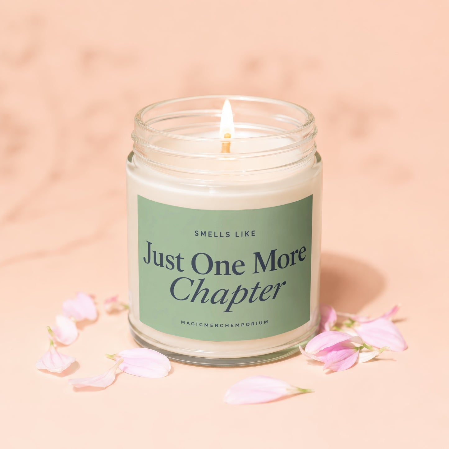 Lit candle with "Just One More Chapter" text on a green label, surrounded by petals.