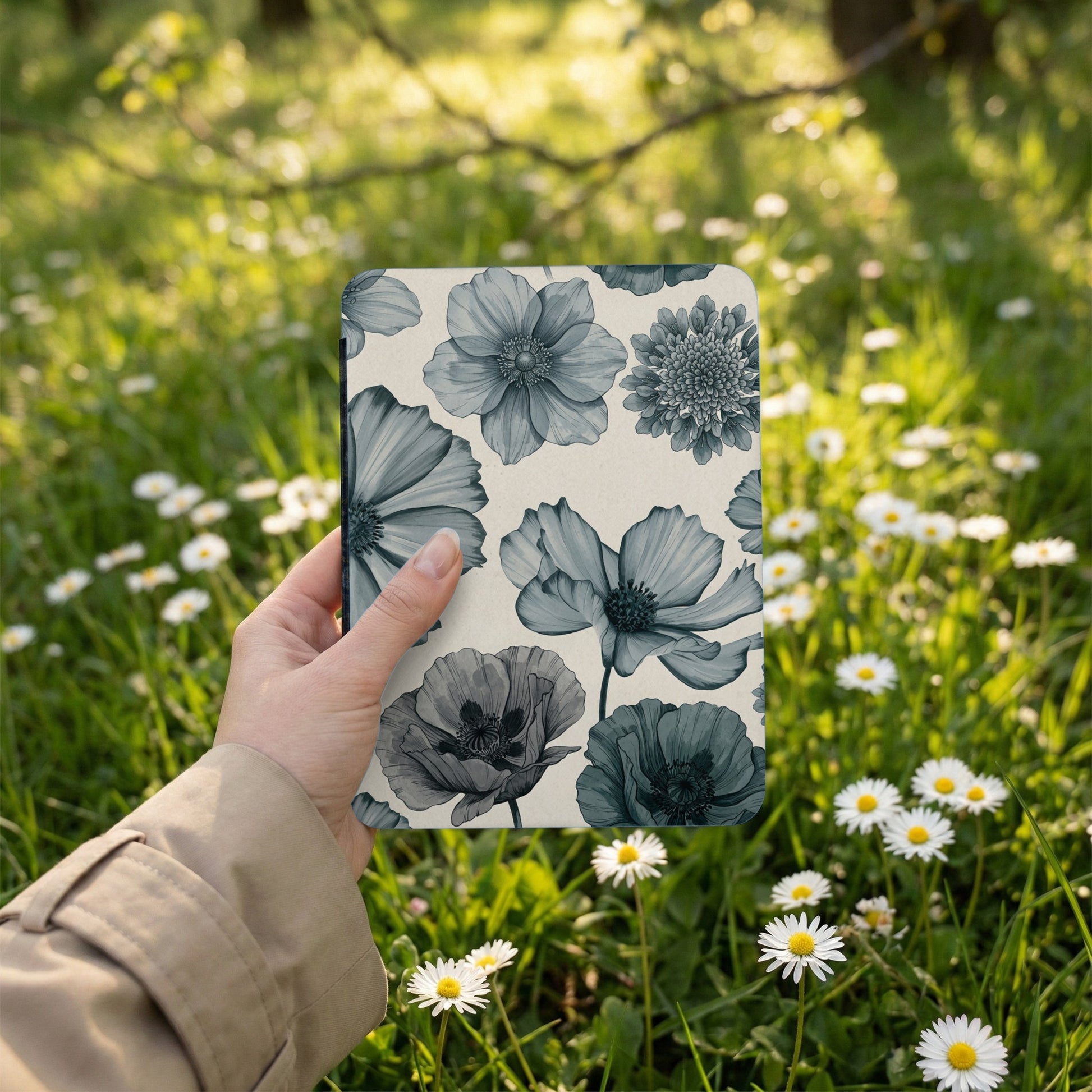 Hand holding notepad with blue floral pattern amongst daisies and grass