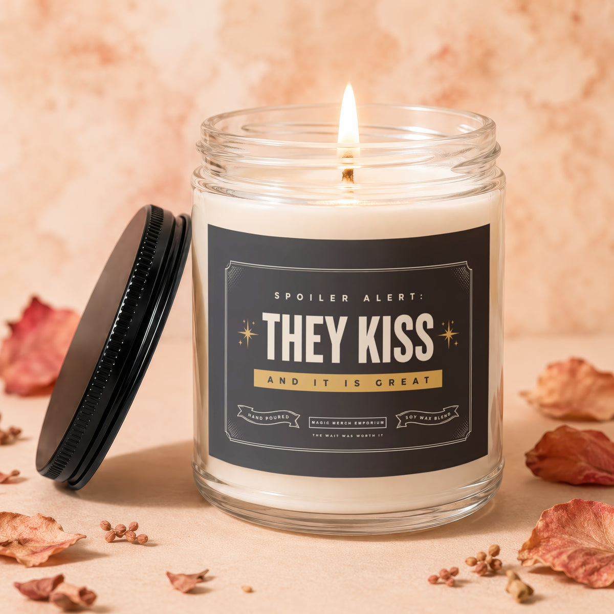 Burning candle in glass jar with "SPOILER ALERT: THEY KISS AND IT IS GREAT" label.