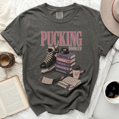T-shirt with ice skates, hockey stick, and stacked books with "Pucking Booked" text.
