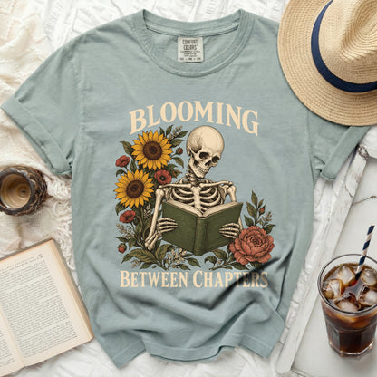 Skeleton reading a book surrounded by flowers with text "Blooming Between Chapters".