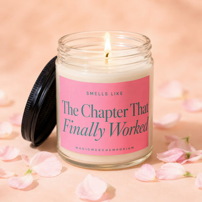Glass candle with pink label reading "The Chapter That Finally Worked" surrounded by petals.
