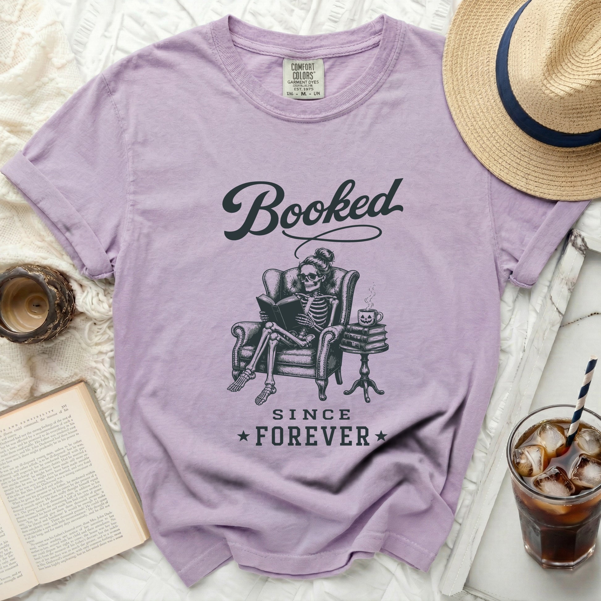 Lavender t-shirt with "Booked Since Forever" graphic of skeleton reading