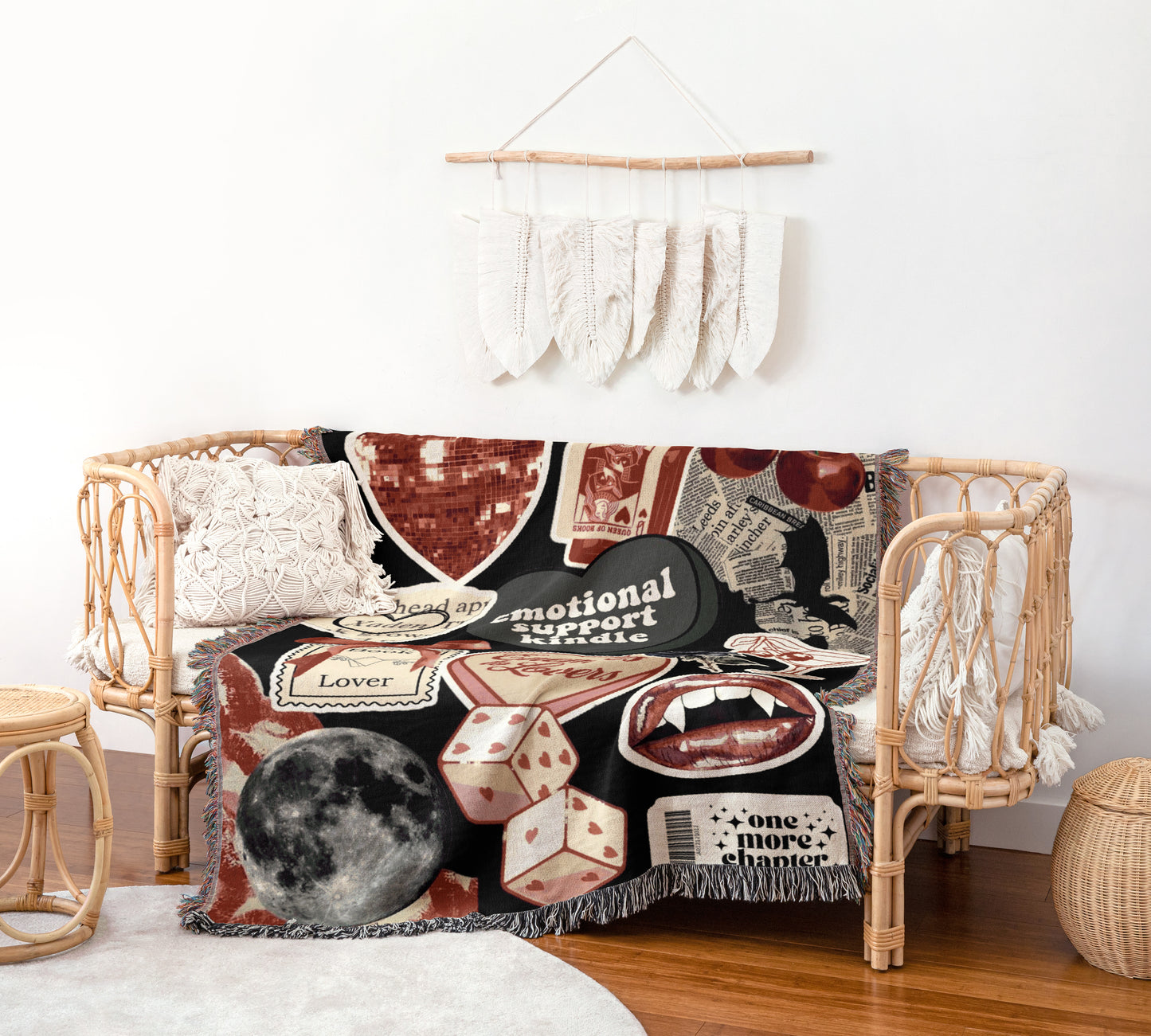 a cozy living room with a woven bench and a decorative wall hanging. The bench is adorned with a colorful blanket that includes various text and images, such as a moon, a heart, and a skull. The wall hanging consists of white feathers arranged in a decorative pattern. The room also includes a small table and a woven basket, creating a warm and inviting atmosphere.