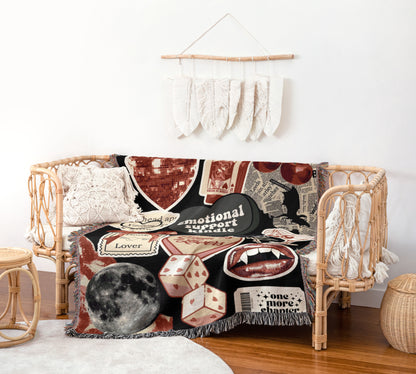 a cozy living room with a woven bench and a decorative wall hanging. The bench is adorned with a colorful blanket that includes various text and images, such as a moon, a heart, and a skull. The wall hanging consists of white feathers arranged in a decorative pattern. The room also includes a small table and a woven basket, creating a warm and inviting atmosphere.
