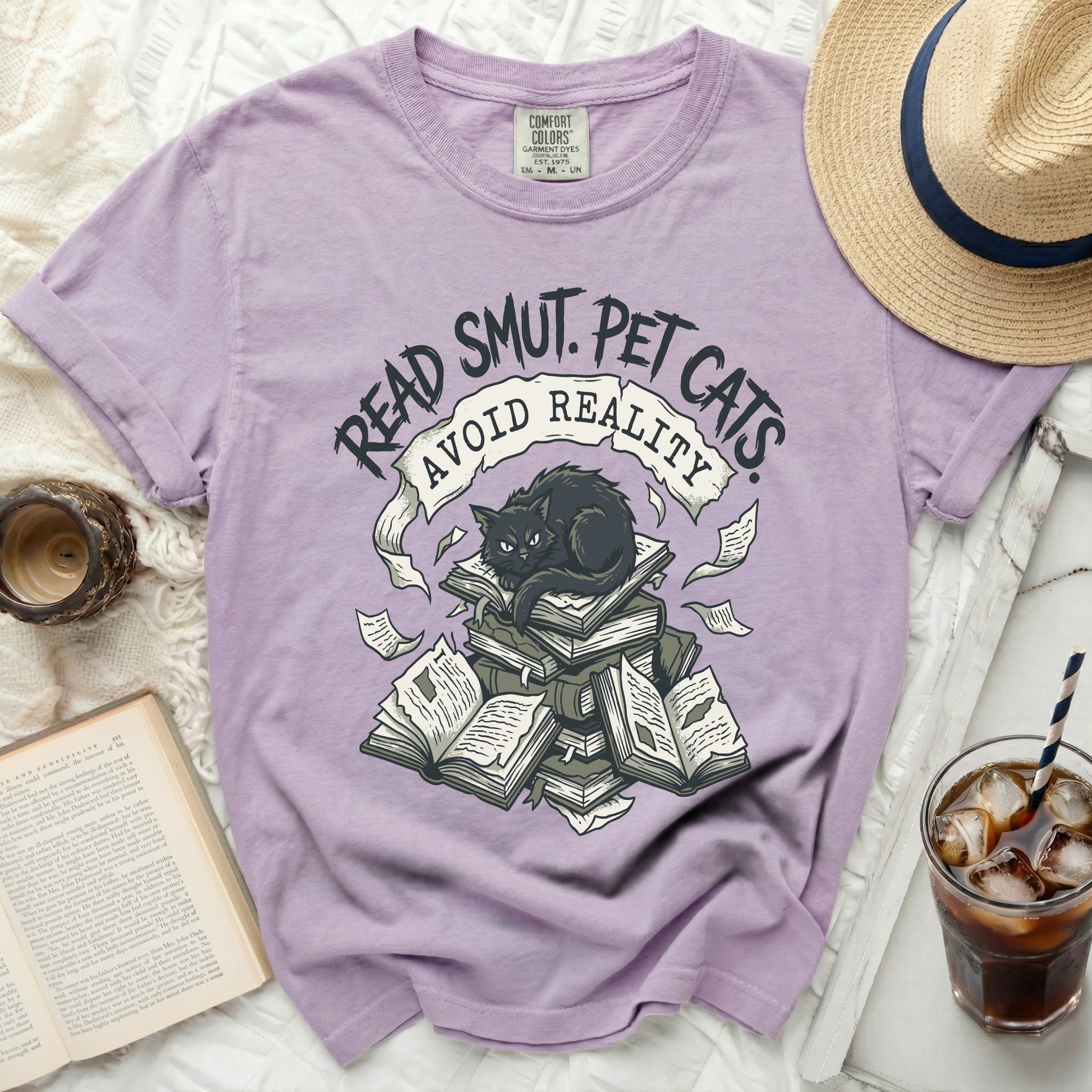 Purple t-shirt with graphic of black cat on books, text "Read Smut. Pet Cats. Avoid Reality."