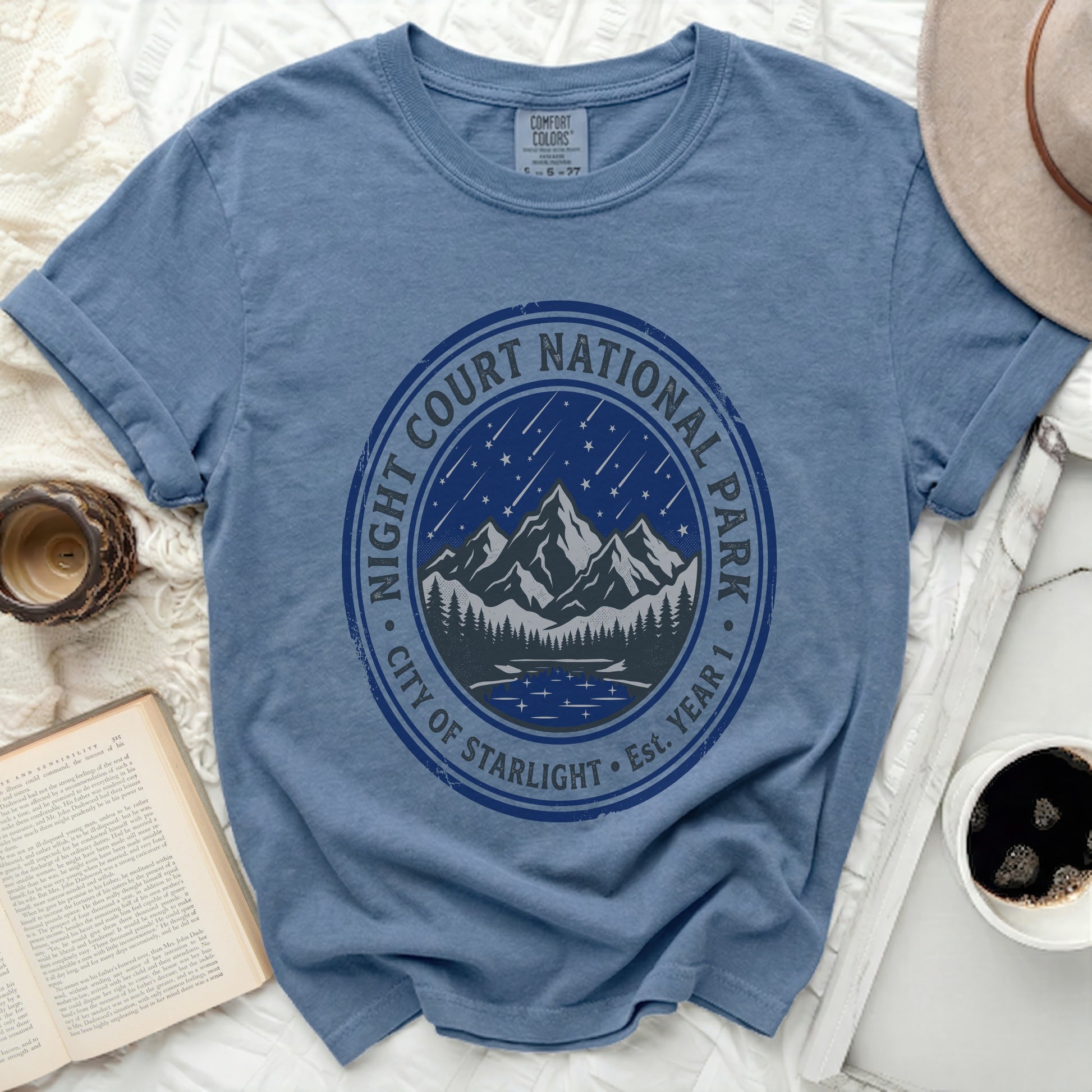 Blue t-shirt with a circular graphic of mountains, trees, a lake, and falling stars.