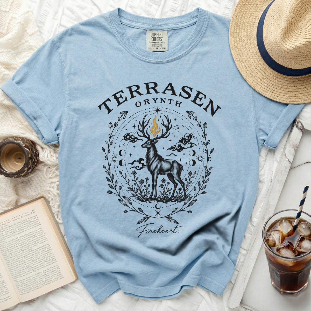 Light blue t-shirt featuring a black and gold graphic of a stag with floral and celestial motifs.