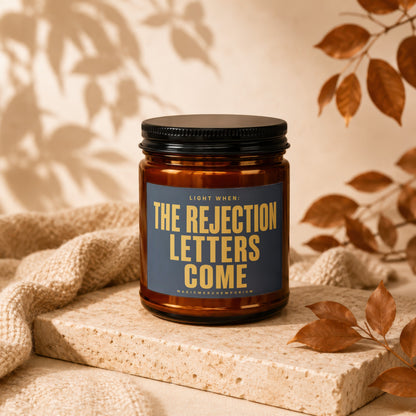 Amber jar candle with dark blue label reading "Light When: The Rejection Letters Come".