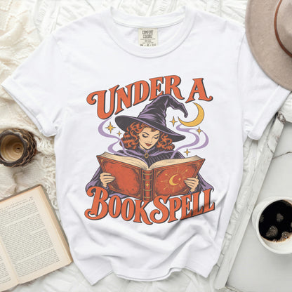 White t-shirt with "Under a Book Spell" graphic of a witch reading a book.